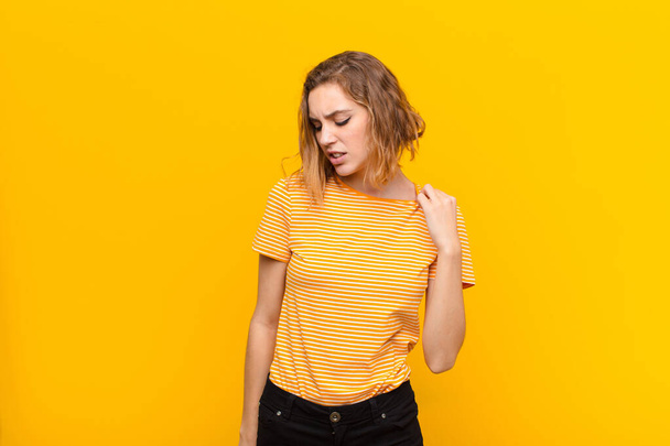 young blonde woman feeling stressed, anxious, tired and frustrated, pulling shirt neck, looking frustrated with problem against flat color wall - Valokuva, kuva