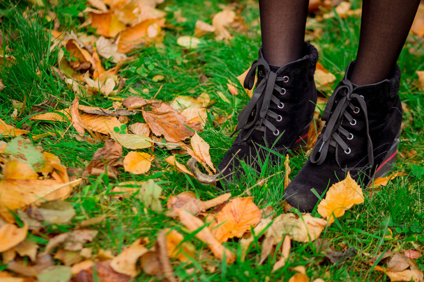Πτώση φύλλωμα, κορίτσι με τα πόδια στο πράσινο γρασίδι με κίτρινα φύλλα, μπότες - Φωτογραφία, εικόνα
