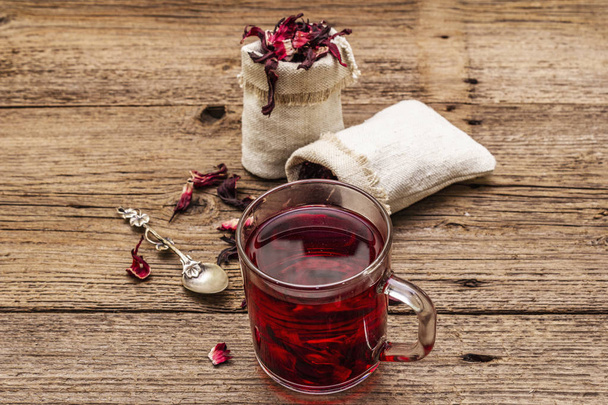 Hot hibiscus tea. Dry petals, linen sacks. Healthy food and self-care concept. Old wooden boards backgrounds - Photo, Image