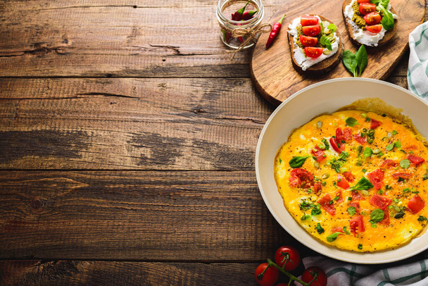 gezond ontbijt van omelet met kerstomaten en spinazie in koekenpan en toast met kwark, pestosaus en kerstomaten - Foto, afbeelding
