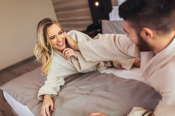 Paar in badjassen liggend op bed in hotelkamer. - Foto, afbeelding