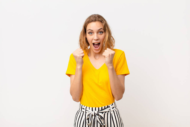 young blonde woman feeling shocked, excited and happy, laughing and celebrating success, saying wow! against flat color wall - Foto, Imagem