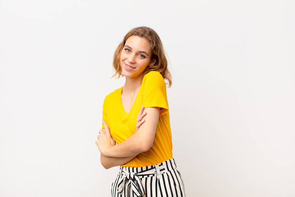 young blonde woman laughing happily with arms crossed, with a relaxed, positive and satisfied pose against flat color wall - Фото, зображення