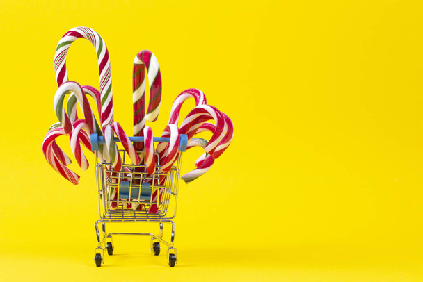 Mini carrello della spesa con bastoncini di zucchero natalizio su sfondo giallo
 - Foto, immagini