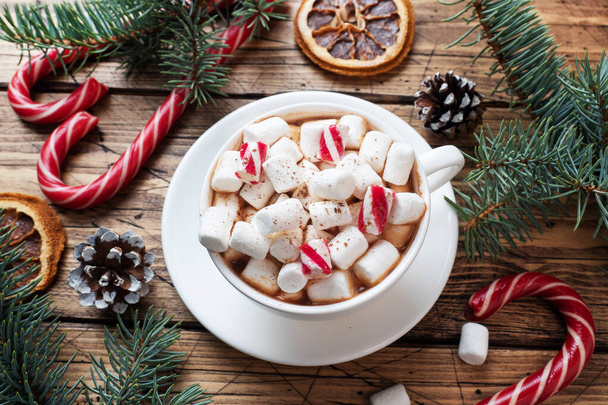 A Cup of hot chocolate with marshmallows. Christmas tree and decorations, cane caramel and oranges nuts Wooden background - Fotoğraf, Görsel