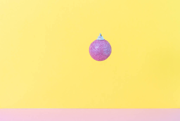 Ροζ παγωμένη χριστουγεννιάτικη μπάλα σε κίτρινο και ροζ φόντο. 3d σύνθεση. Νέο έτος και γενέθλια έννοια. Κενό διάστημα για κείμενο.  - Φωτογραφία, εικόνα