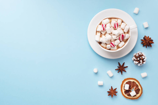 Xícara de chocolate quente com cacau em pó de marshmallow e nozes de caramelo, laranjas em fundo azul pastel com espaço de cópia. Conceito de inverno Natal
. - Foto, Imagem