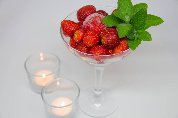 gefrorene Erdbeeren mit Minzblättern im Glas und Kerzen auf weißem Hintergrund - Foto, Bild