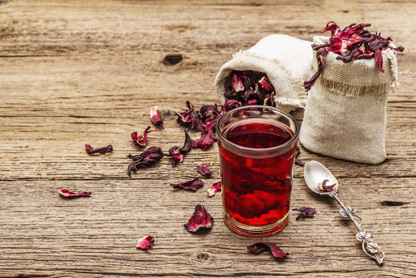 Hot hibiscus tea. Dry petals, linen sacks. Healthy food and self-care concept. Old wooden boards backgrounds - Foto, Imagem