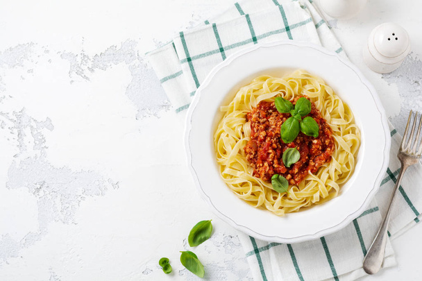 Traditional Italian dish fettuccine pasta with bolognese sauce, basil and parmesan cheese in a white plate on a light wooden background. Top view. - Photo, image