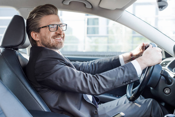 happy bearded ambassador holding steering wheel while driving car  - Photo, Image