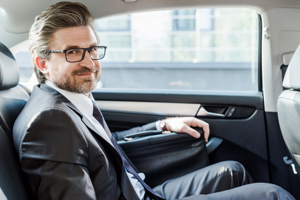 χαρούμενος διπλωμάτης σε γυαλιά κάθεται με το χαρτοφύλακα στο αυτοκίνητο - Φωτογραφία, εικόνα