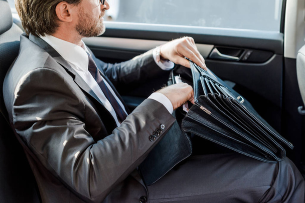 Ausgeschnittene Ansicht eines Diplomaten, der Aktentasche hält und im Auto sitzt - Foto, Bild