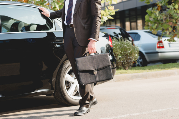 cropped view of diplomat standing with briefcase near car  - Фото, изображение