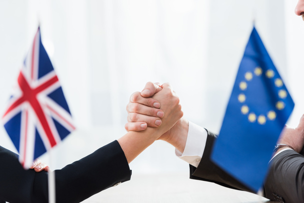 przycięty widok ambasadorów trzymających się za ręce w pobliżu Unii Europejskiej i flagi zjednoczonego Królestwa  - Zdjęcie, obraz