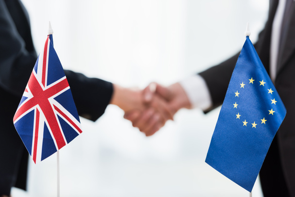 обрезанный вид послов, пожимающих руки возле Европейского союза и флагов Соединенного Королевства
  - Фото, изображение