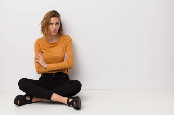 young blonde woman feeling displeased and disappointed, looking serious, annoyed and angry with crossed arms against flat color wall - Foto, afbeelding