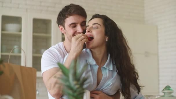 Young couple flirting at home. Smiling man and woman eating strawberry. - 映像、動画