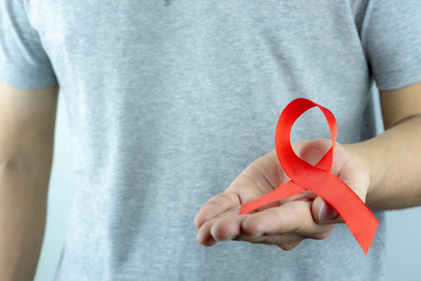 Pomaga świadomość, męskie dłonie trzymające czerwoną wstążkę świadomości AIDS. Wo. - Zdjęcie, obraz