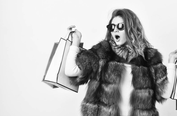 Girl wear sunglasses and fur coat shopping white background. Lady hold shopping bags. Discount and sale. Buy with discount on black friday. Shopping with promo code. Woman shopping luxury boutique - Photo, Image