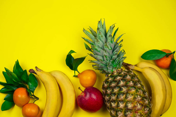 top view fresh tropical fruits layout pineapple,bananas, apple and tangerines on a yellow background - Foto, Imagem