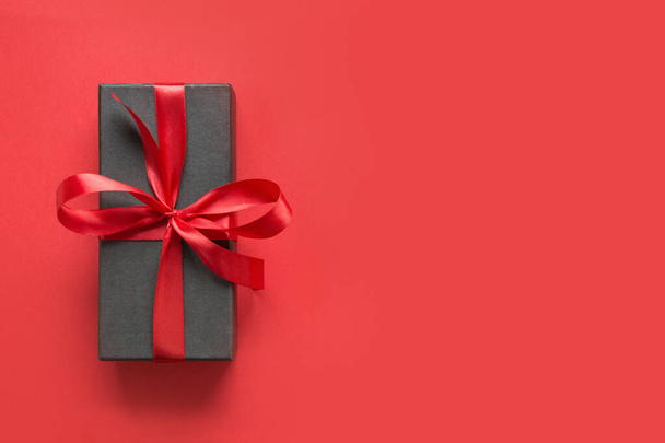 Black gift box wrapped with red ribbon on red surface. - Foto, Imagen