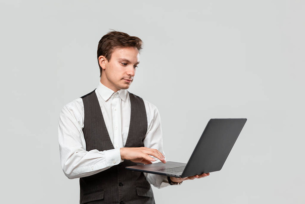 Успешный бизнесмен держит ноутбук изолированным на сером фоне
 - Фото, изображение
