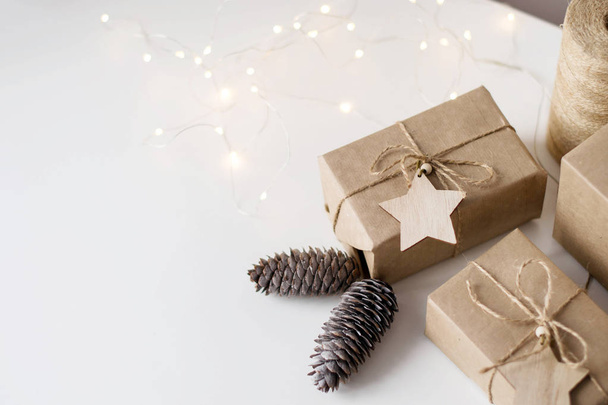 Gifts in Kraft paper on white background. Decor fir cones, wooden stars, jute rope. Copy space. - Foto, Imagen