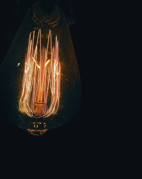 A vertical closeup shot of a light bulb on a black background - Foto, afbeelding