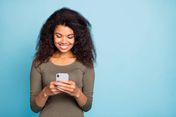 Portrait of positive cheerful afro american girl use her cellphone have online conversation in social media network read feednews wear casual style green pullover isolated over blue color background - Photo, image