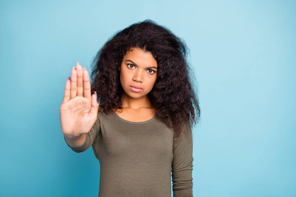 Portrait of serious confident mulatto girl hold hand palm say it is forbidden reject choice decision solution wear green casual style pullover isolated over blue color background - 写真・画像