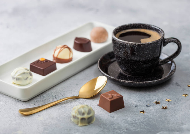 Luxury Chocolate candies in white porcelain plate with cup of black coffee and golden spoon on light table background. - Фото, зображення