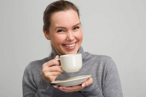 Νεαρή ευτυχισμένη γυναίκα απολαμβάνει ένα φλιτζάνι καφέ ή τσάι - Φωτογραφία, εικόνα