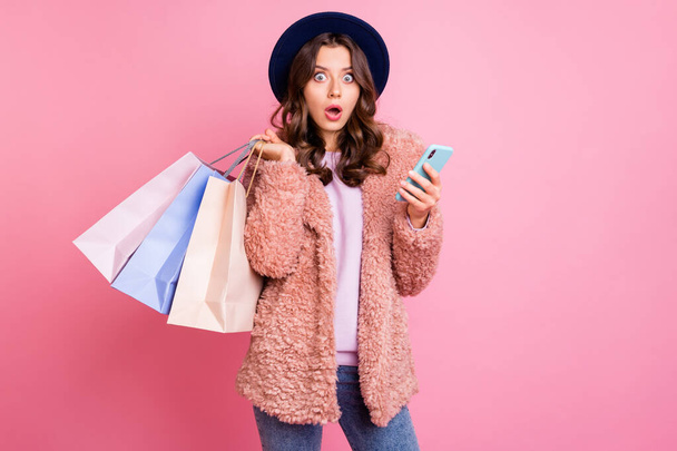 Photo of pretty millennial lady hold many packs telephone reading unexpected negative comments wear stylish fluffy jacket trendy retro blue hat isolated pink background - Foto, immagini