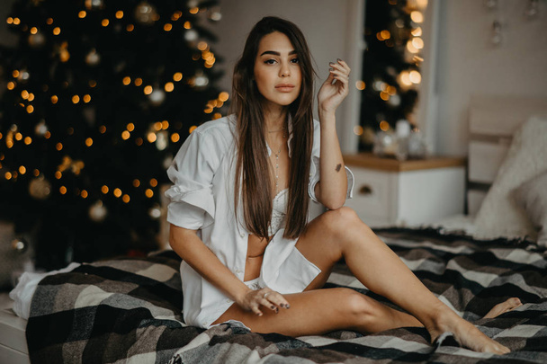 Mladá žena sedí na posteli na pozadí vánočního stromečku - Fotografie, Obrázek