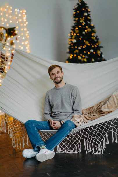 L'uomo felice si siede in amaca sullo sfondo dell'albero di Natale
. - Foto, immagini