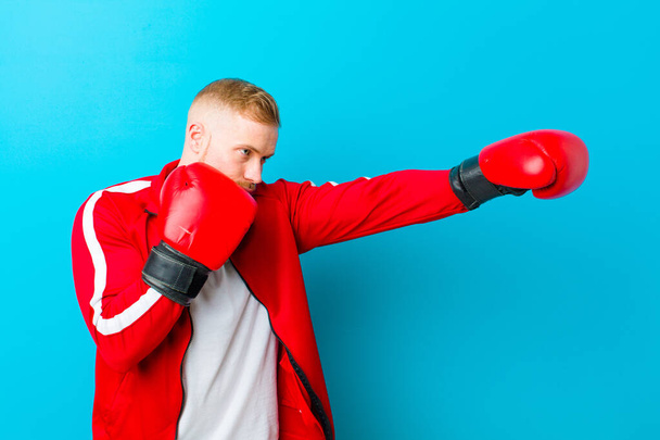 young blonde man wearing sports clothes  against blue background. fitness concept - Foto, Imagem