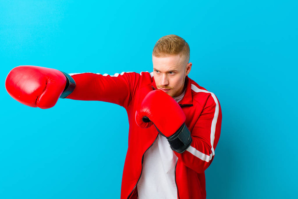 young blonde man wearing sports clothes  against blue background. fitness concept - Foto, afbeelding