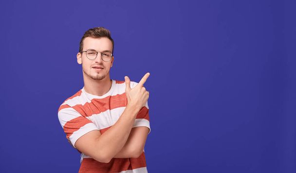 A young guy in casual clothes and glasses shows a finger to the side. - Foto, afbeelding