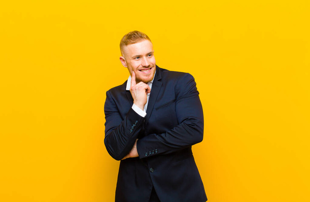 young blond businessman smiling happily and daydreaming or doubting, looking to the side - Foto, Imagen