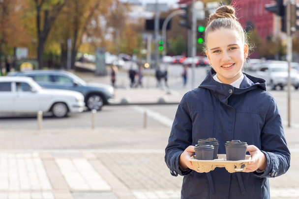 Teenager girl is walking along a city street with cups of tea and coffee for friends. - Foto, Bild