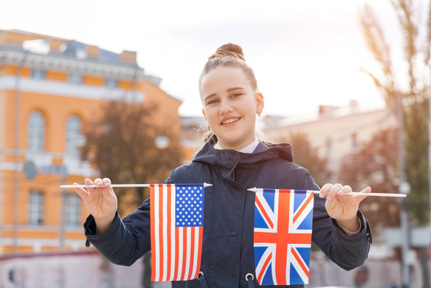 Chica adolescente con dos banderas de Estados Unidos y Reino Unido en un fondo de la calle de la ciudad. Aprender inglés en el extranjero
. - Foto, Imagen