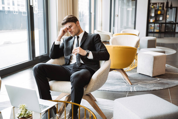 Photo of tired businessman wearing suit sitiing on armchair with - Photo, Image