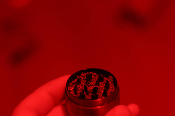 Nahaufnahme-Mühle mit Marihuana in der Hand. Ansicht von oben. Rotlicht. Kopierraum und verschwommener Hintergrund. medizinische Verwendung von Medikamenten. Platz für Text über Unkraut - Foto, Bild