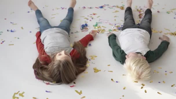 A gyerekek hóangyalokat csinálnak a fehér padlón konfettivel.. - Felvétel, videó