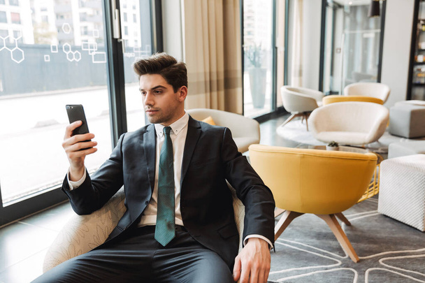 Young serious businessman indoors in business center office using mobile phone. - Foto, imagen