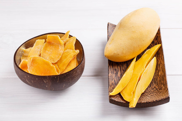Зневоднені скибочки манго та свіжий сирий манго на дерев'яній тарілці на w
 - Фото, зображення