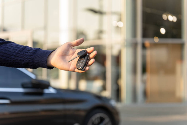 Hand with keys from a luxury black car on the background of the dealership. Dealership of rent, hire cars. Carsharing - Fotó, kép