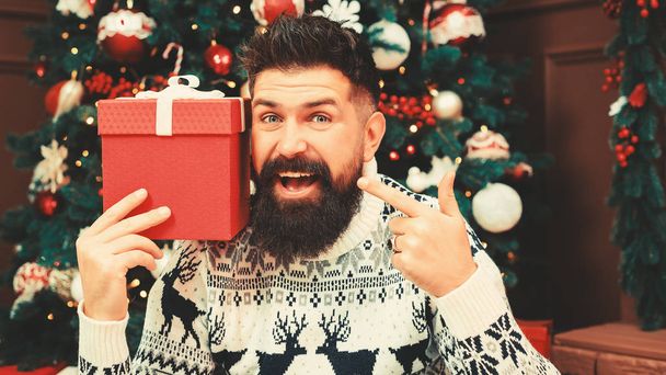 Bearded guy with christmas gift. Handsome man in sweater sitting near christmas tree. Christmas celebration, gifts and sales - Foto, immagini