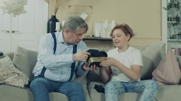 Senior man is putting on VR-glasses with his grandsons advice - Filmati, video